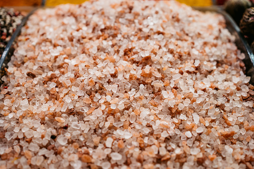 View of the rock salt crystals falling from a measuring cup over a brown wooden background