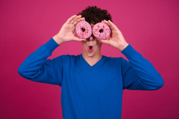 istock Young attractive guy eats pink donuts. Delicious breakfast and good vibes. 1590033054