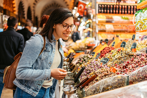 Young woman looking at spices and dried tea leaves at the Grand Bazaar In Kapali Carsi in Istanbul, Turkey.