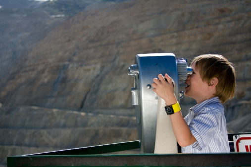 Six year old boy views an open pit mine through coin operated binoculars.