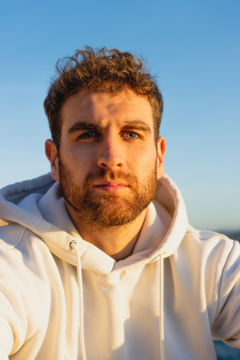 Portrait of blond, blue-eyed handsome man in white sweatshirt looking at camera