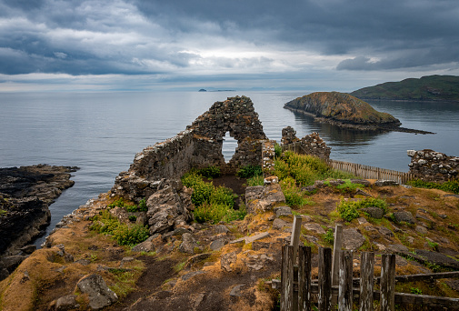 Scenic coastline in the Isle of Skye, Scotland with ruins on hill overlooking the ocean and small island.