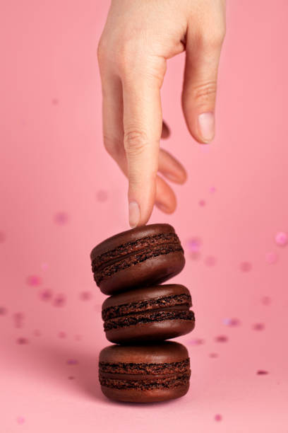 istock Three chocolate macaroons and a woman's hand on a pink background 1590093079