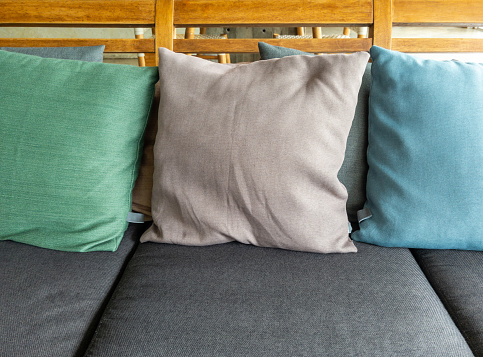 The soft textile cushion in the pastel color on the gray textile sofa in the living room of the modern house, front view with the copy space.