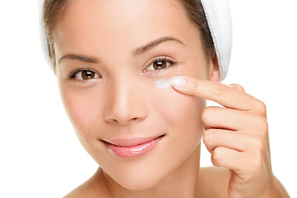 Face cream woman Face cream woman applying skin cream under eyes. Beauty eye contour cream, wrinkle cream or anti-aging skin care cream. Beautiful young mixed race Asian Chinese beauty model in her 20s isolated on white background. Similar: asian eyebrows stock pictures, royalty-free photos & images
