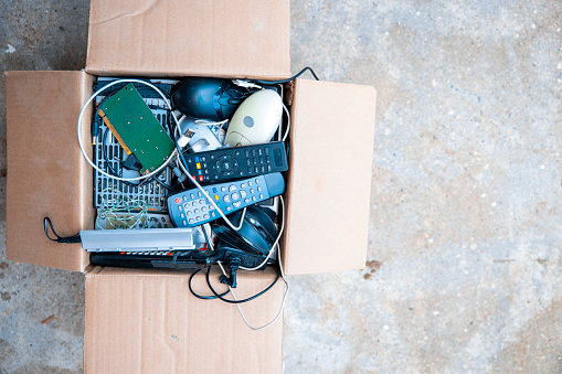 Old used technology devices on pile in carton box. Above view, copy space