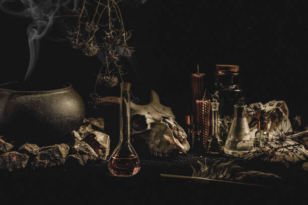 Witchcraft or alchemistry altar. Goats skull, flasks, dry herbs, iron cauldron, wax candles, smoking incense in the dark, low key, selective focus. Religion, cult, occultism, magic concept