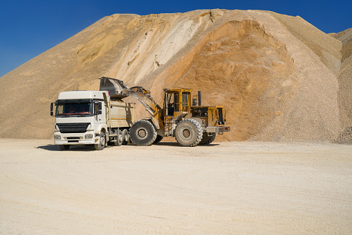 Backhoe loading sand into truck at quarry at work