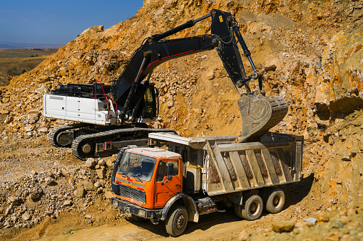 Hydraulic crawler excavator loading stone into truck in quarry at work