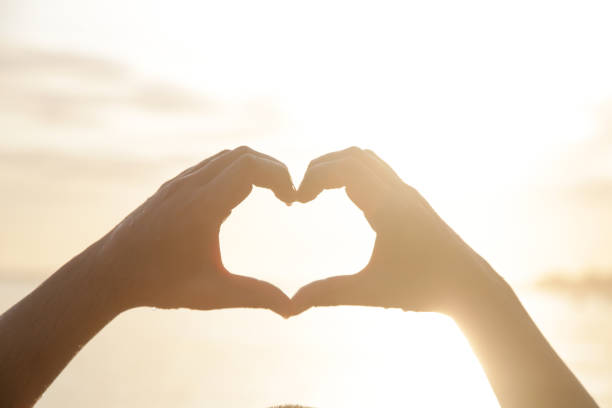 istock Man creating the shape of a heart with hands at the beach during sunset 1590141622