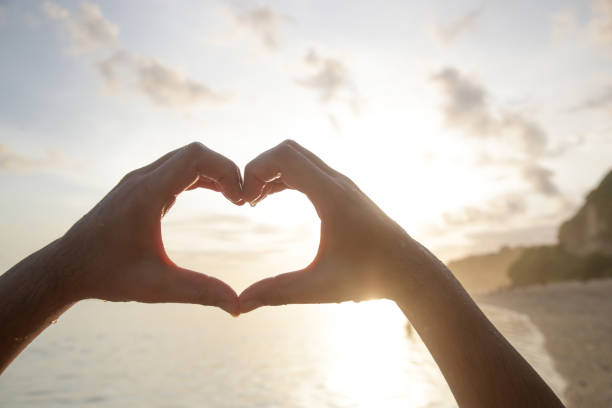 istock Man creating the shape of a heart with hands at the beach during sunset 1590148046