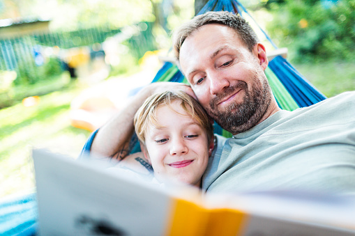 Father with son relaxing in hammock reading book