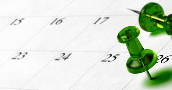 green pushpin pointing on the number 26 of a calendar with room for text at the left side of the image