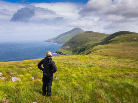 A woman standing close to the coastline on Achill Island, Ireland, looking out over the sea.