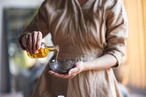 Close up shot of an anonymous woman working at the spa, holding a bottle and sipping oil into a bowl ready for a massage.