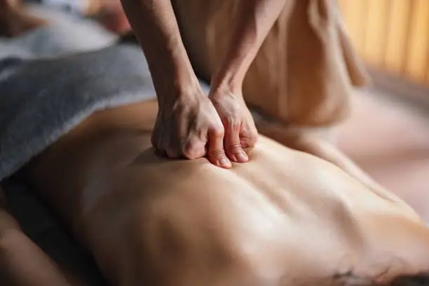 An unrecognizable masseuse giving a relaxing massage to an anonymous woman lying face down on the bed.