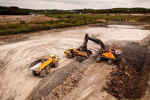 Aerial view directly above a crane or mechanical digger with grab loading a dumper truck with earth and soil in the construction industry on a brownfield site with copy space