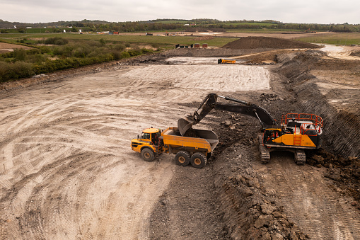 Aerial view directly above a crane or mechanical digger with grab loading a dumper truck with earth and soil in the construction industry on a brownfield site with copy space