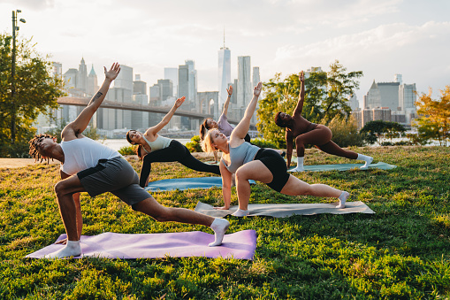 Yoga class in the city at sunset with New York City skyline in the background. Multiethnic group of people. Active and healthy lifestyle concept.