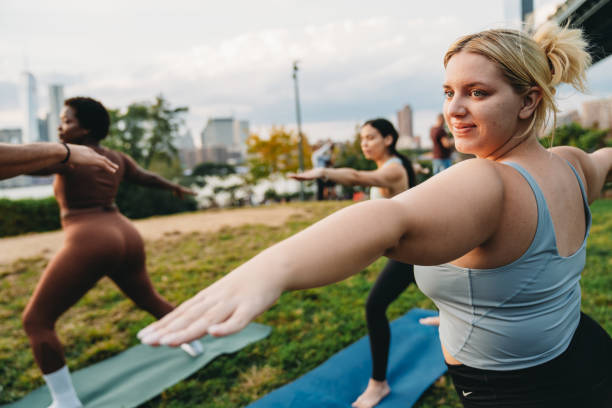 un groupe multiethnique de personnes pratique le yoga en plein air dans la ville au coucher du soleil avec la ligne d’horizon de new york en arrière-plan - yoga class caucasian young adult group of people photos et images de collection