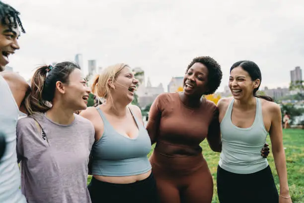 Photo of A multiethnic group of people is embracing together after an exercise class in the city