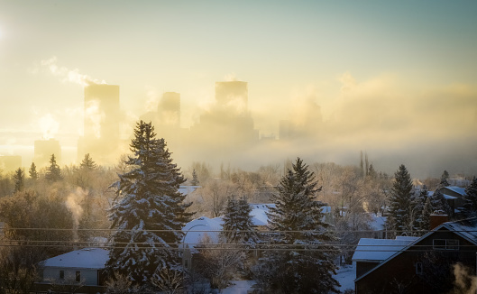 A thick layer of fog is covering the Calgary skyline on this frigid winter morning in Alberta, Canada. Snow is on the ground and roofs, and the sun shin is shining through the haze.