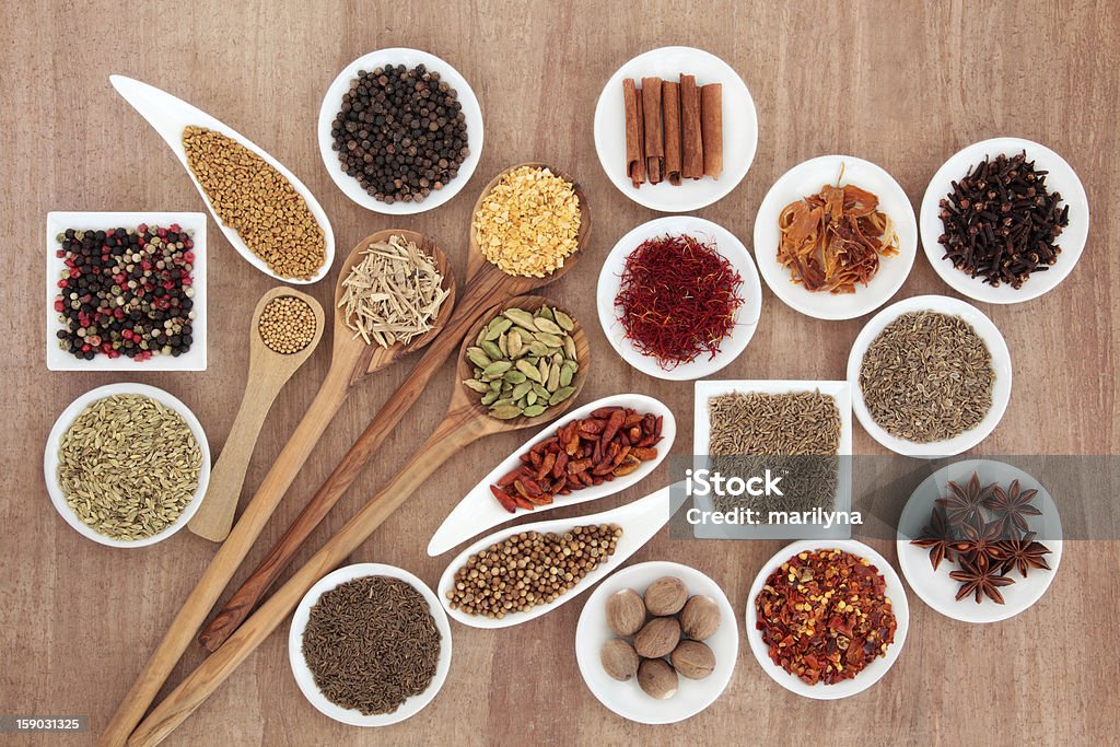 Spice and Herb Selection Large herb and spice selection in white bowls and wooden spoons over papyrus background. Black Peppercorn Stock Photo