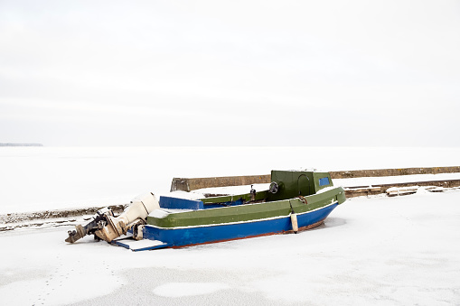 Old lonely motorboat in a frozen harbour in winter, snowy landscape, plenty of copy space on top
