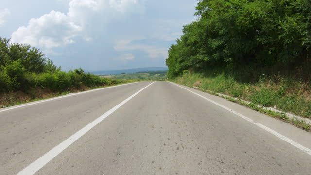 A car or motorcycle driving very fast along the winding road to the top of the mountain and then descends down to a large valley with agricultural fields. Blue sky with clouds. POV shot