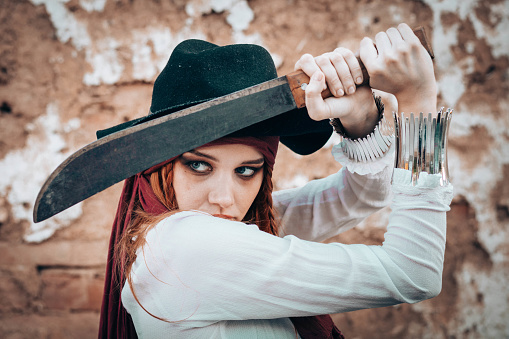 Outdoor portrait of young female in pirate costume with a machete
