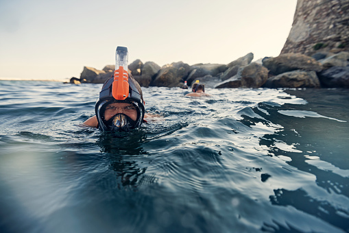 Teenagers snorkeling with full-face snorkel masks in clean waters of Ligurian sea in the town of Rapallo.\nThey are swimming in a small bay next to the Castello di Rapallo and a small beach.\nShow with Canon R5