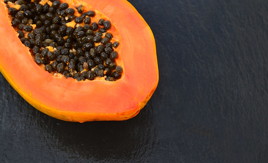 Fresh ripe organic papaya tropical fruit cut in half on a black stone background.Healthy eating,diet or vegan food concept.Selective focus.