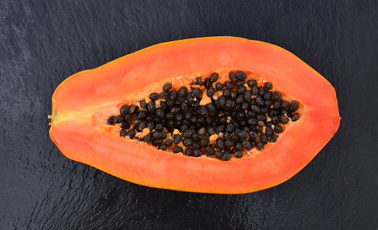 Fresh ripe organic papaya tropical fruit cut in half on a black stone background.Healthy eating,diet or vegan food concept.Selective focus.