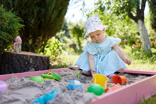cute little girl playing in sand in sandbox with various toys on outdoor playground