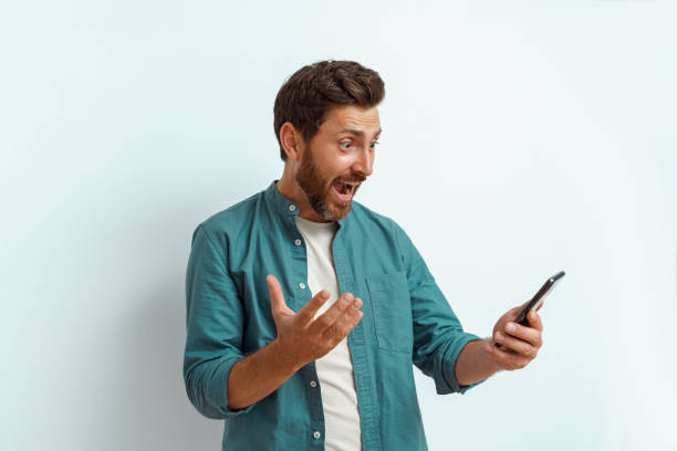 istock Surprised man showing happy gesture while looking to his mobile phone on white background 1590548315