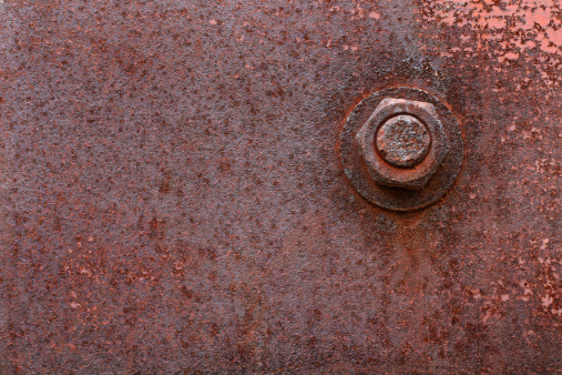 A rusty nut and bolt on an old rusty weathered metal plate.