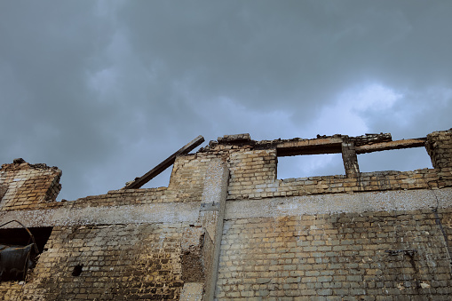 Damaged brick wall of an industrial building on a grey cloudy background. Roof collapsed after a fire. Heap of building debris.