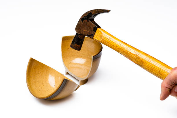 Hand of man with hammer broken  a ceramic bowl of brown color..Conceptual image of violence.Image made in studio