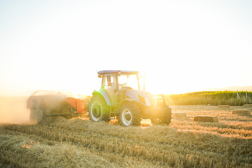 man making bales with tractor and machine in big field at sunset