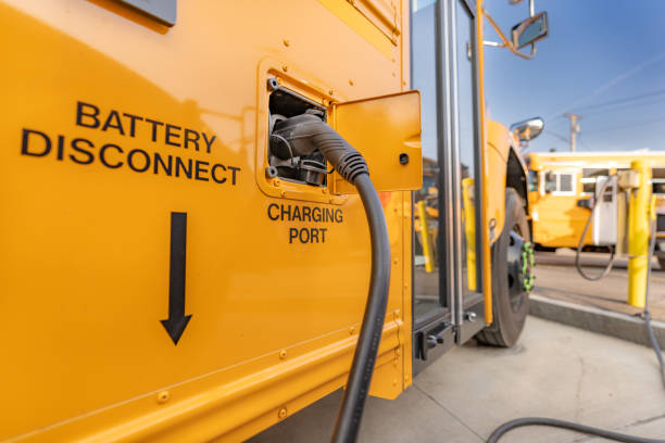 ônibus escolar elétrico amarelo conectado a uma estação de carregamento. - autocarro elétrico - fotografias e filmes do acervo