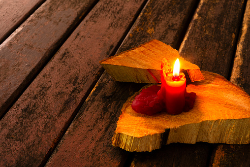 Red candle with flame over rustic wood table ay late afternoon at home. Dangerous situation to have a candle with flame over wood.