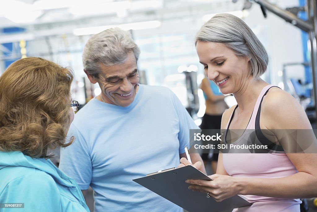 Casal sênior falando com uma mulher na academia de ginástica - Foto de stock de Academia de ginástica royalty-free