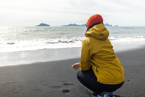 Female tourist dressed in warm clothes enjoying exploring the black sand beach