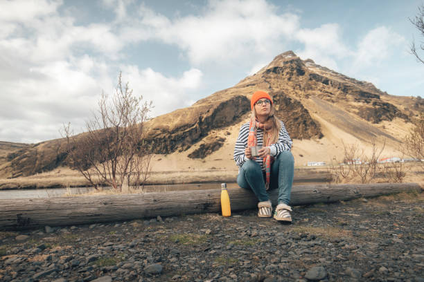 Female tourist sits on a tree trunk in nature and enjoys the view. Iceland