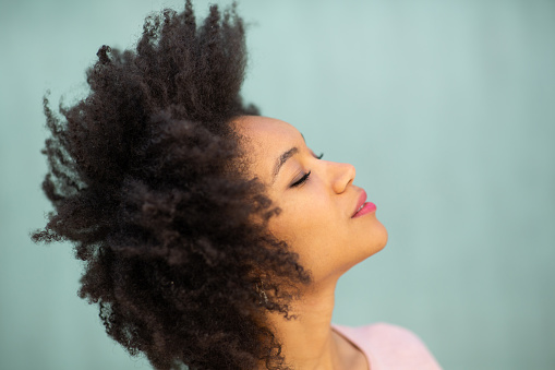 Close up side portrait of attractive young african american woman with afro hair and eyes closed against blue background