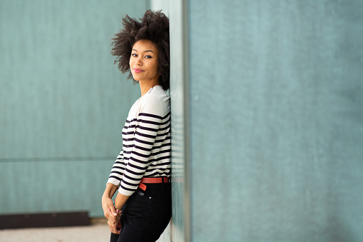 Portrait of attractive young african woman leaning to wall and looking at camera