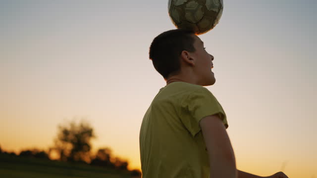 SLO MO Young Soccer Player Practicing Heading the Ball under Orange Sky at Sunset