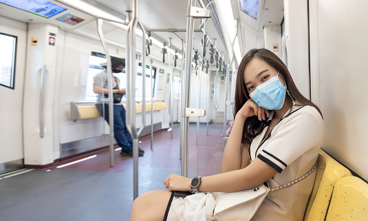 Always wearingmedical mask when living in public place and transportation and keep distance from everyone. Asian businesswoman model show wearing mask on skytrain in urban transport to protect pandemic.