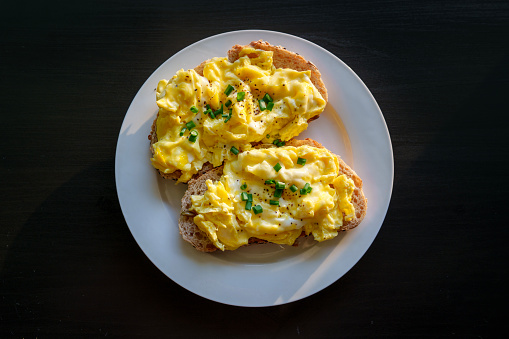 a white square plate for breakast with eggs, bananas and toast bread on a wooden table background