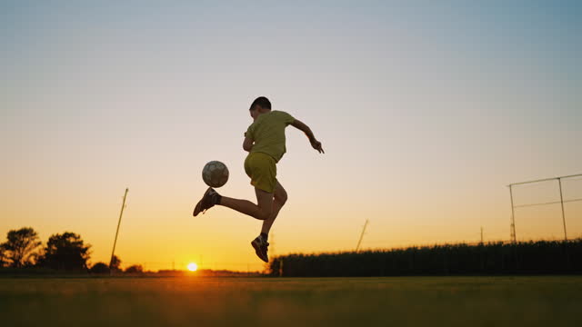 SLO MO Boy Showing Football Trick in Field at Sunset